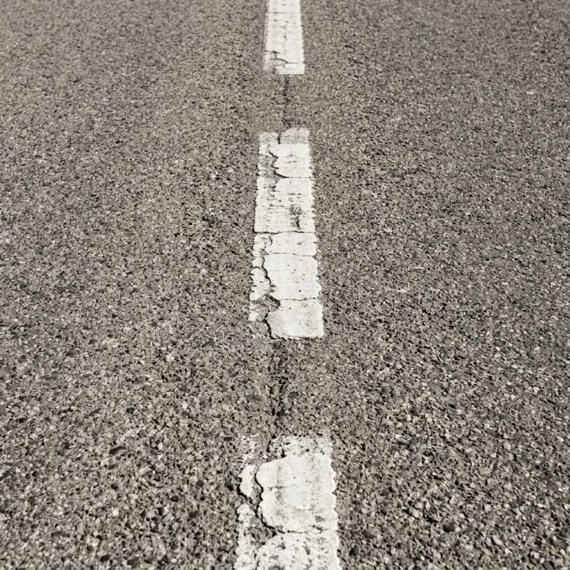 Close-up of a cracked white dashed road marking on gray asphalt