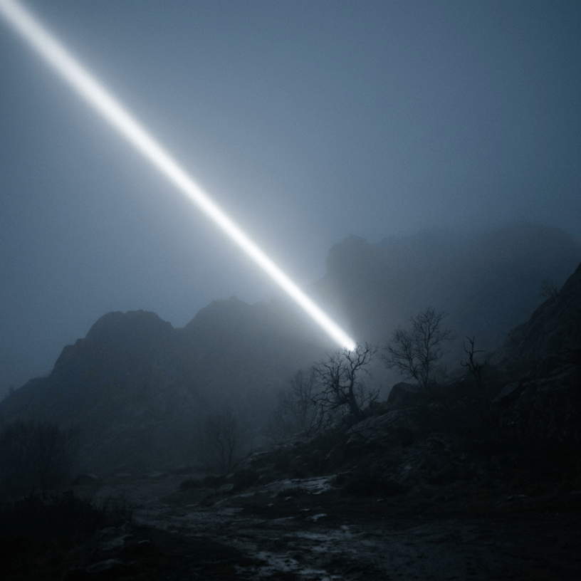 Bright diagonal beam of light shining through fog above rocky mountain terrain