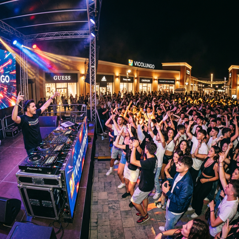 DJ performing on stage with a large crowd dancing and enjoying the night event
