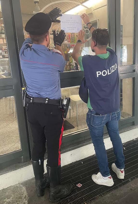 Un Carabiniere e un agente di Polizia affiggono il provvedimento di sospensione della licenza all’ingresso di un locale.