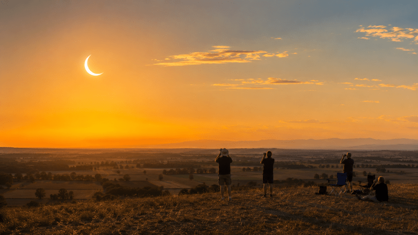 Eclissi parziale di Sole del 12 agosto 2026 osservata al tramonto dalla campagna piemontese, con alcune persone rivolte verso l’orizzonte.