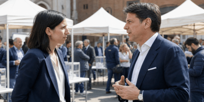 Elly Schlein e Giuseppe Conte dialogano davanti ad alcuni gazebo elettorali allestiti in una piazza italiana.