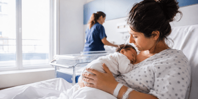 Madre con il suo neonato in braccio dopo il parto, in una luminosa stanza di maternità ospedaliera.