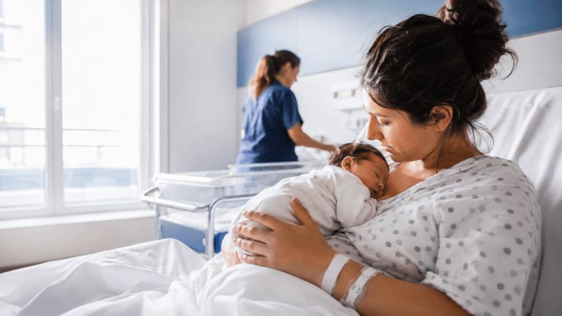 Madre con il suo neonato in braccio dopo il parto, in una luminosa stanza di maternità ospedaliera.