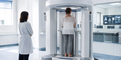 Paziente in piedi durante un esame con TAC Cone Beam in un moderno reparto di diagnostica, sotto la supervisione di una specialista.