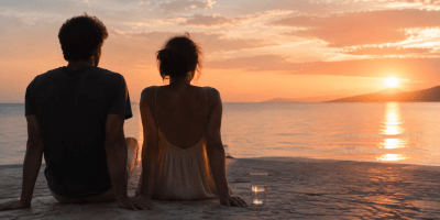 Due persone sedute di fronte al mare al tramonto, con un bicchiere d’acqua accanto.