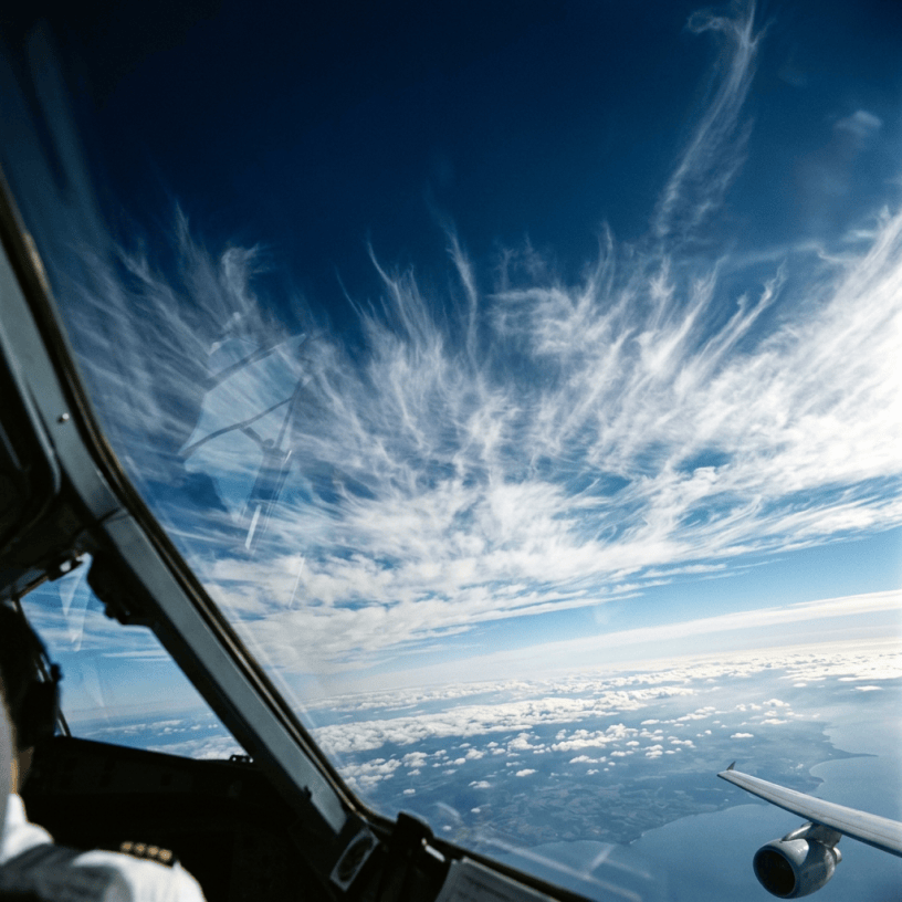 View from airplane cockpit showing clouds, coastline, and aircraft wing