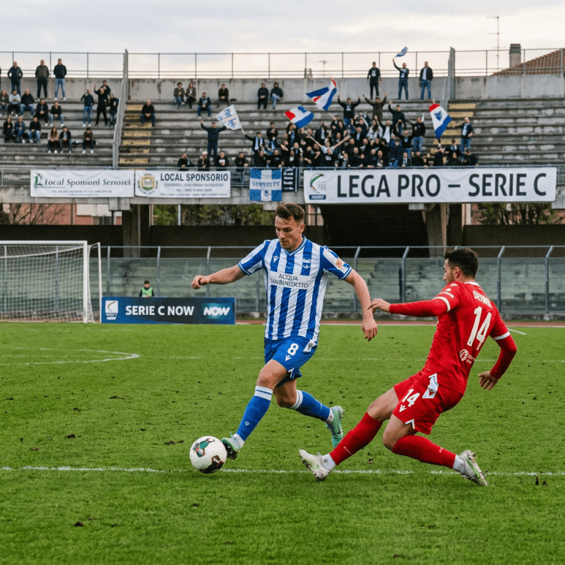 Two soccer players contest the ball in front of cheering supporters and Serie C signs