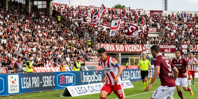 Vicenza player dribbling past Reggiana defenders during a crowded football match