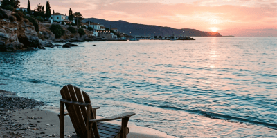 Wooden chair on a pebbly beach facing a sunset over calm sea