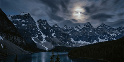 Moonlit alpine lake surrounded by snow-capped mountains and evergreen trees