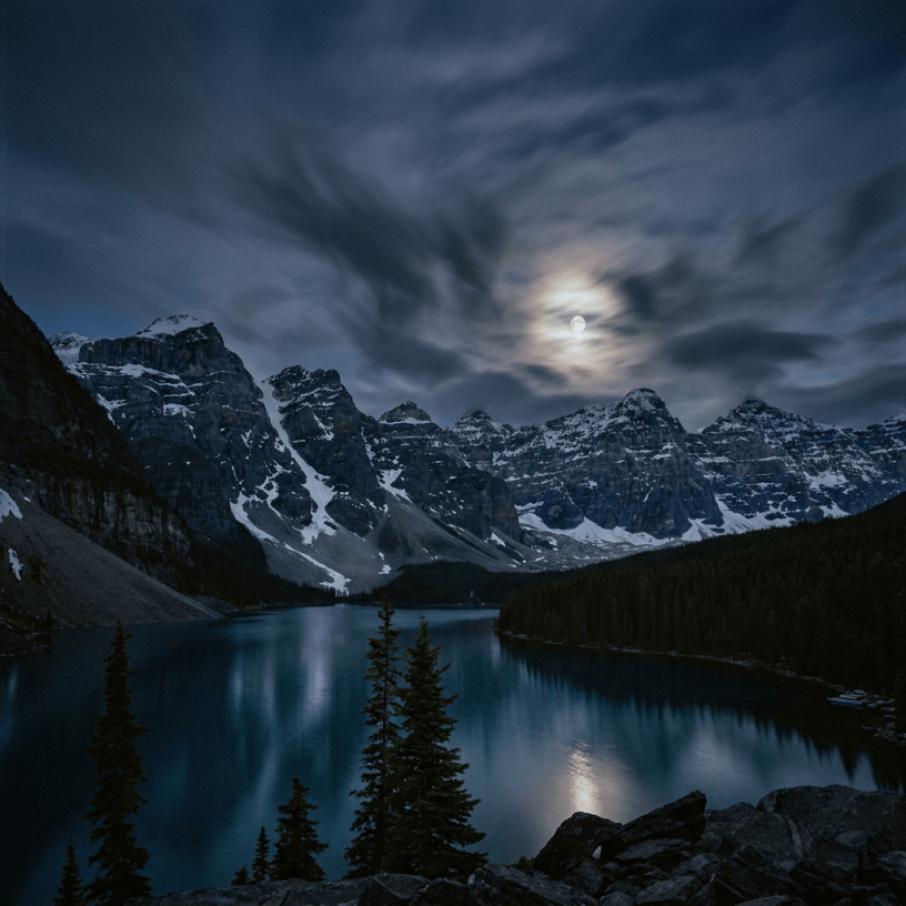 Moonlit alpine lake surrounded by snow-capped mountains and evergreen trees