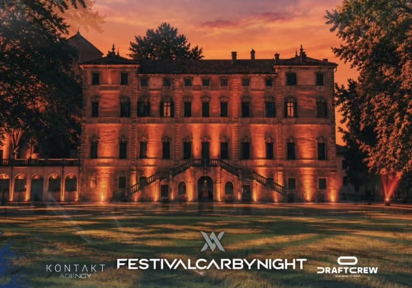 An illuminated historic building at dusk, showcasing warm lighting and surrounded by trees, with event branding at the bottom.