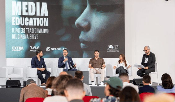 A panel discussion titled 'Media Education' featuring five speakers seated on stage, with a backdrop displaying the event title and themes related to the transformative power of short films.