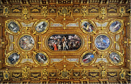 Intricately decorated ceiling featuring gold embellishments and several painted scenes in oval frames, showcasing historical or mythical subjects.