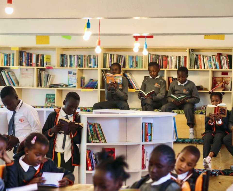 Children reading books in a bright library setting, with shelves filled with books and colorful lighting.