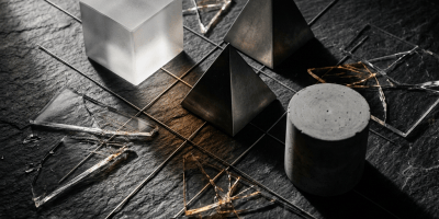 Geometric sculptures and fragmented glass arranged on a dark stone surface