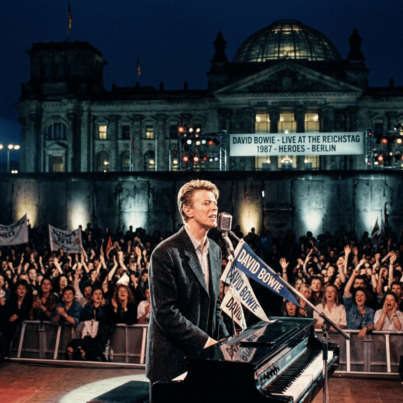 David Bowie performs before Reichstag; banner reads “DAVID BOWIE - LIVE AT THE REICHSTAG 1987 - HEROES - BERLIN.”