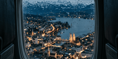 Rain-speckled airplane window overlooking a lakeside city and snow-capped mountains